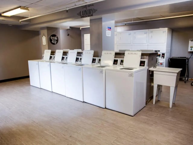 Row of white washing machines sink and dryers laundry room at Auden Ithaca in Ithaca Student Accommodation