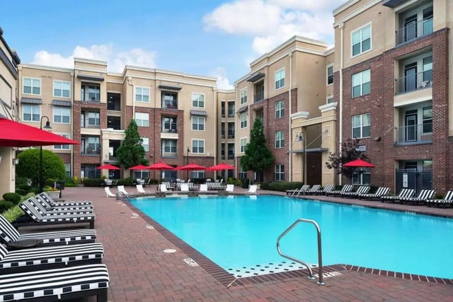 Pool lounge chairs red umbrellas apartment building exterior at The Crimson in Tuscaloosa Student Accommodation