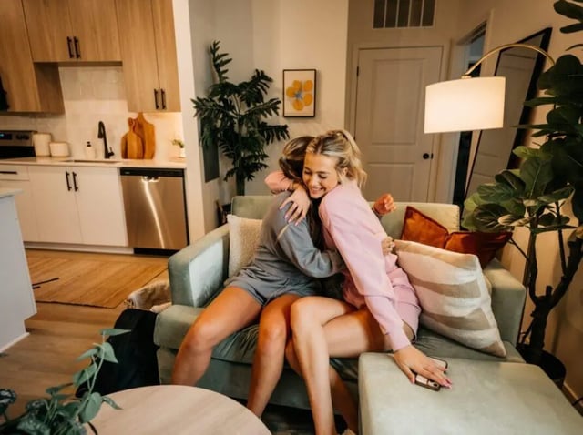 Two young women hugging on sofa kitchen living room at Rambler Athens in Atlanta Student Accommodation