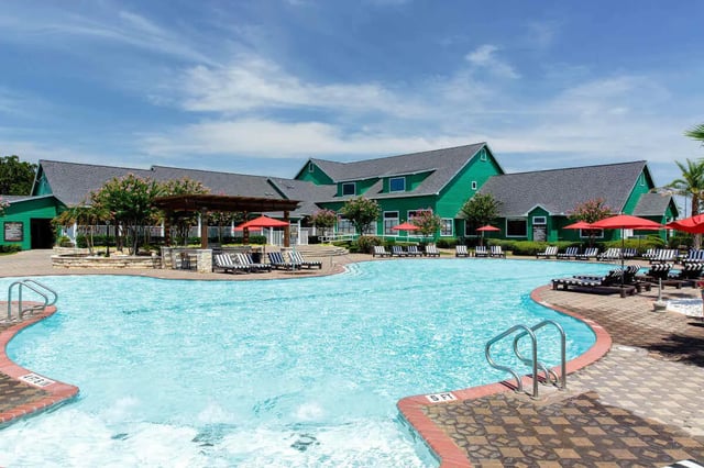 Pool lounge chairs umbrellas green buildings exterior at The London in College Station Student Accommodation