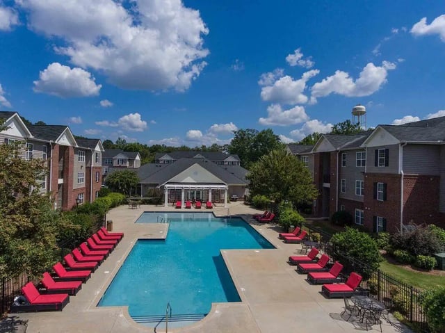 Apartment buildings with pool and red lounge chairs exterior at The Reserve in Carrollton Student Accommodation