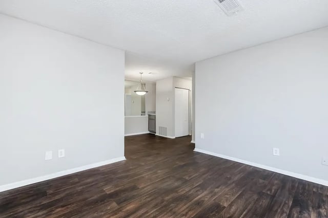Empty room with dark wood floors and kitchen view living room at Villas Del Mirasol in Roswell Student Accommodation