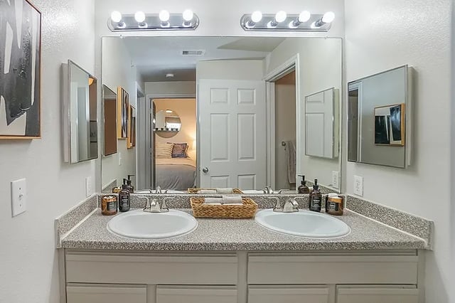 Double sinks in vanity with basket and bedroom beyond bathroom at The Leonard Denton in Denton Student Accommodation