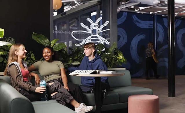Students on couch with book plant wall art living room at Parkway Gate in Manchester Student Accommodation