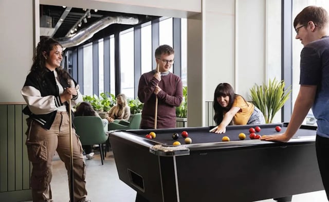 Students playing pool table with cues in common area at Parkway Gate in Manchester Student Accommodation