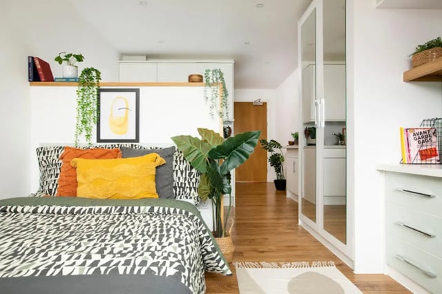 Bed with pillows plants and kitchen area Bedroom at Tramworks in Glasgow Student Accommodation