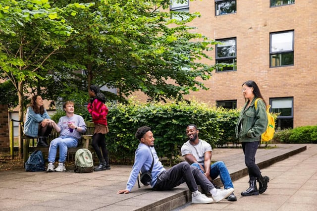 Students socializing outdoors near brick building exterior at Tramworks in Glasgow Student Accommodation