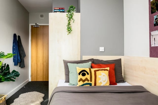 Bed with colorful pillows wardrobe and plant bedroom at Phoenix Court in Bristol Student Accommodation
