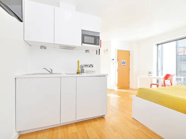 White kitchen cabinets sink microwave and yellow bed living room at The Pavilion - Leeds in Leeds Student Accommodation