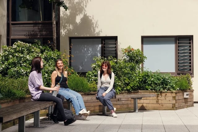 Three students relax on benches exterior at Newgate Court in Newcastle Upon Tyne Student Accommodation