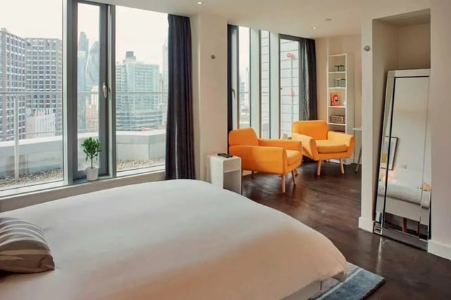 Bed orange chairs white shelf mirror bedroom at Chapter Aldgate in London Student Accommodation
