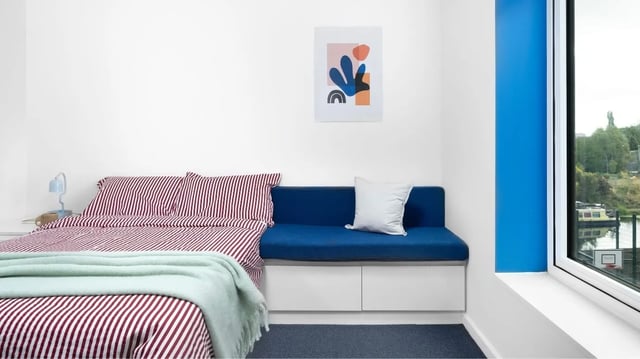 Bed with striped bedding blue bench white pillow bedroom at Scape Mile End in London Student Accommodation