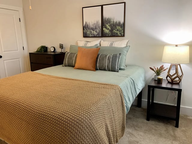 Bed with tan blanket pillows dresser and lamp bedroom at The Retreat West in Orlando Student Accommodation