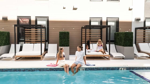 Students relaxing by pool with cabanas and loungers pool area at NOVA Tallahassee in Tallahassee Student Accommodation