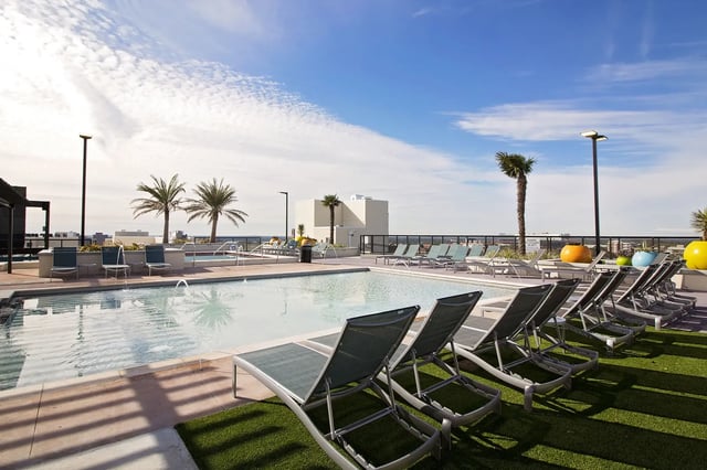 Pool lounge chairs palm trees and building exterior at The Standard at Gainesville in Gainesville Student Accommodation