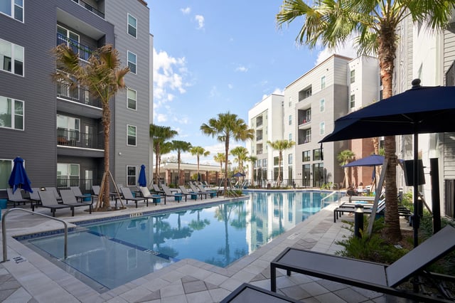 Pool lounge chairs palm trees and apartment buildings exterior at The Accolade Collegiate Village West in Orlando Student Accommodation