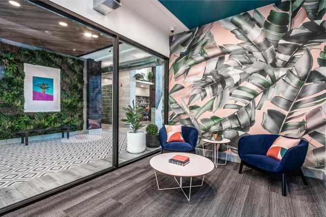 Blue chairs leafy wall art and plants lounge area at The Aves @ Twelve 100 in Orlando Student Accommodation