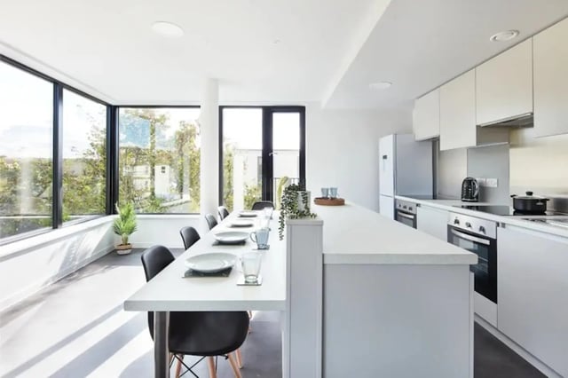 Dining table with place settings and modern kitchen. at Ravilious House in Brighton Student Accommodation
