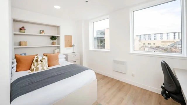 Bed with orange pillows shelves desk and chair bedroom at Discovery Studios in Dundee Student Accommodation