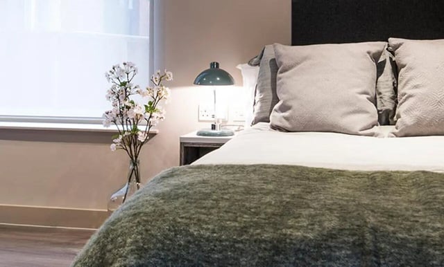 Bed with pillows bedside lamp flowers bedroom at Collegiate Roman House in Derby Student Accommodation