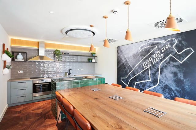 Wooden table orange chairs kitchen artwork communal area at Vita Student Pebble Mill in Birmingham Student Accommodation