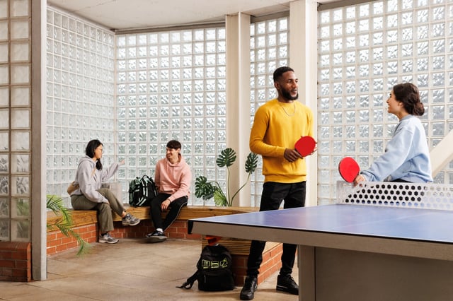 Students playing ping pong with paddles and net living room at Hepworth Lodge in Leeds Student Accommodation