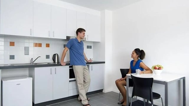 Man by kitchen counter woman at table kitchen at Student Living - 740 Swanston in Melbourne Student Accommodation