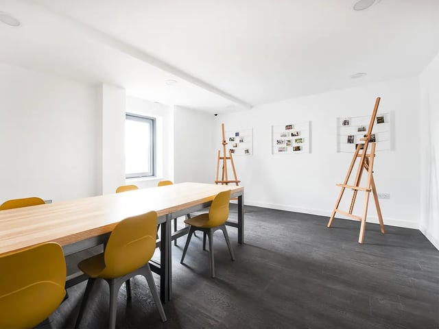 Large table yellow chairs easels on dark floor activity room at Yugo Austen House in Southampton Student Accommodation