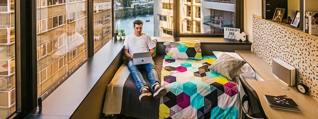 Man with laptop on bed with colorful bedding bedroom at Student One Adelaide Street in Brisbane Student Accommodation