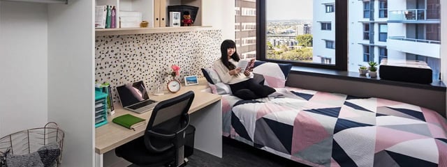 Bed desk laptop and woman reading bedroom at Student One Adelaide Street in Brisbane Student Accommodation