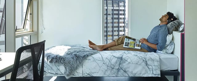 Man listening to music on bed with magazine Bedroom at Student One Wharf Street in Brisbane Student Accommodation