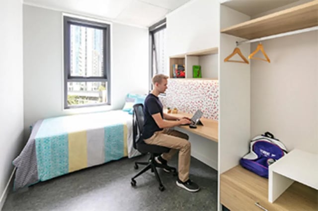 Man working at desk bed closet bedroom at Student One Elizabeth Street in Brisbane Student Accommodation