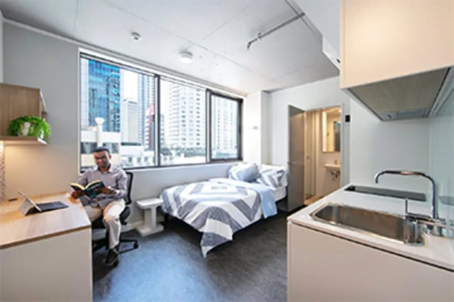 Man reading at desk beside bed kitchen area at Student One Elizabeth Street in Brisbane Student Accommodation