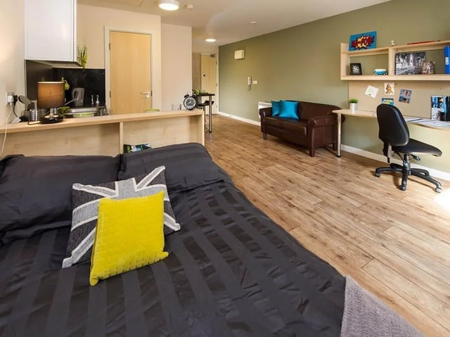 Bed with pillows kitchen area sofa desk Living Room at Optima in Loughborough Student Accommodation
