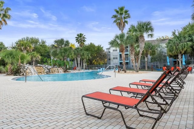 Pool with waterfall lounge chairs and palm trees pool area at Cabana Beach Gainesville in Gainesville Student Accommodation