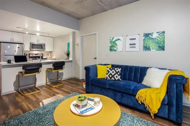 Blue sofa kitchen counter laptop and bar stools living room at Rise At Riverfront Crossings in Iowa City Student Accommodation