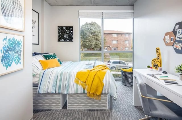 Striped bed with yellow blanket and desk Bedroom at Rise At Riverfront Crossings in Iowa City Student Accommodation