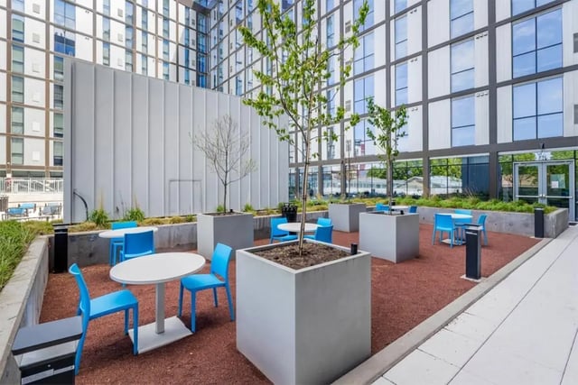 Tables and blue chairs in a courtyard exterior at Rise At Riverfront Crossings in Iowa City Student Accommodation