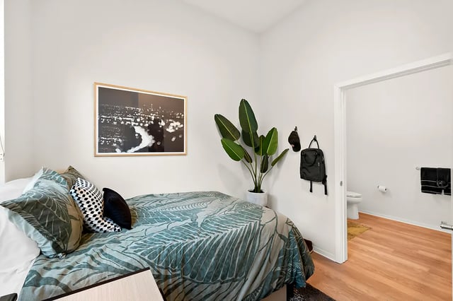 Bed with tropical print bedding plant backpacks bathroom bedroom at Identity Davis Apartments in Davis Student Accommodation