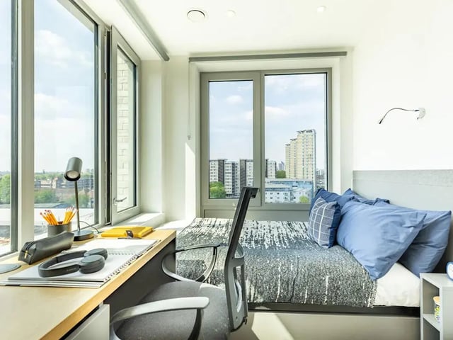 Desk with lamp headphones bed with pillows bedroom at Great Court in London Student Accommodation