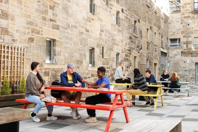 Students sitting at picnic tables outdoors courtyard exterior at Sugarhouse in Edinburgh Student Accommodation