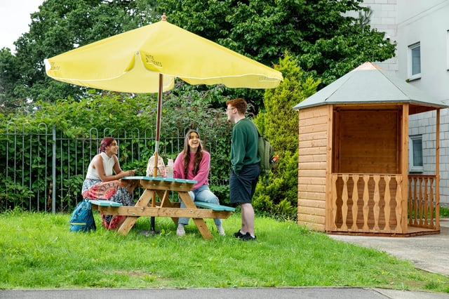 Students at picnic table under umbrella outdoor living area at Clodien House in Cardiff Student Accommodation