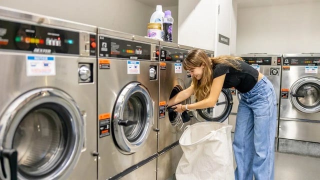 Young woman loading laundry into washing machines laundry room at UniLodge Victoria University in Melbourne Student Accommodation