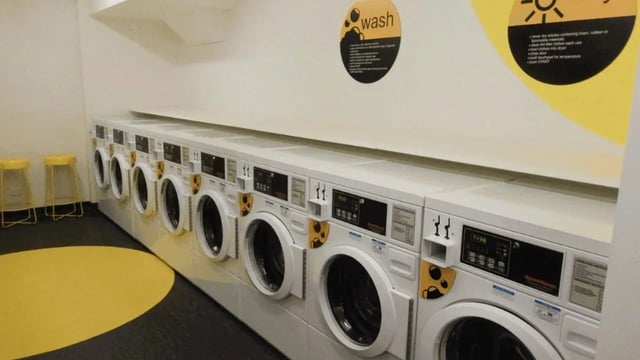 Multiple washing machines and yellow stools laundry room at La Trobe University - Menzies College in Melbourne Student Accommodation