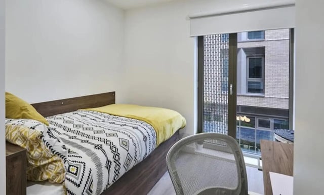 Bed with patterned bedding yellow blanket chair bedroom at The Oaks in Coventry Student Accommodation