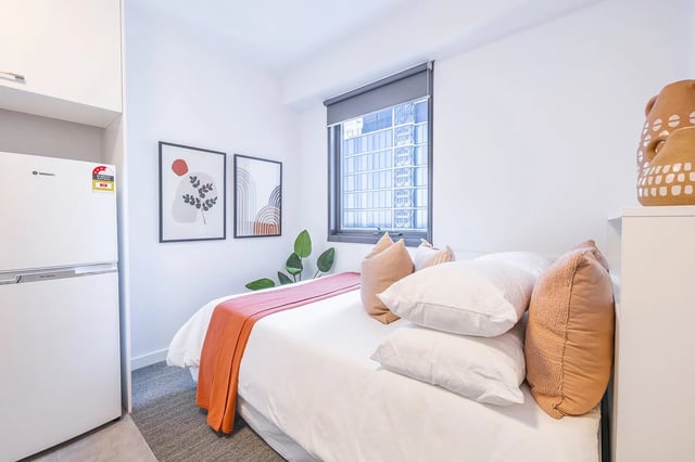 Bed with orange throw artworks and fridge Bedroom at dwell East End Adelaide in Adelaide Student Accommodation