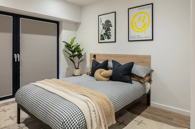 Bed with checkered bedding knot pillow plant bedroom at The Fabric Works in Leeds Student Accommodation