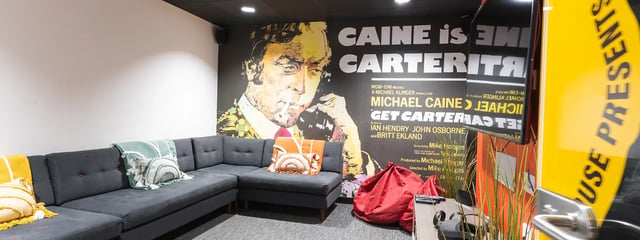 Dark sectional couch with pillows and movie poster living room at Oxford House - Newcastle in Newcastle Upon Tyne Student Accommodation