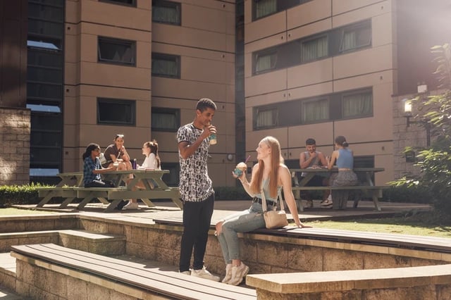 Students sitting at picnic tables outside building exterior at Sir Charles Groves Hall in Manchester Student Accommodation