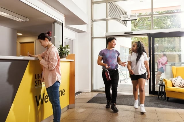 Reception desk student checks in people walk lobby at Sir Charles Groves Hall in Manchester Student Accommodation